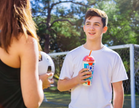 A boy holding an ICEE while talking to a girl holding a soccer ball