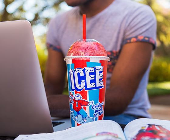 A man studying with a laptop and textbook while drinking an ICEE