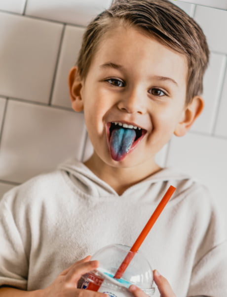 A child holding an ICEE and sticking out his tongue, colored blue from the ICEE